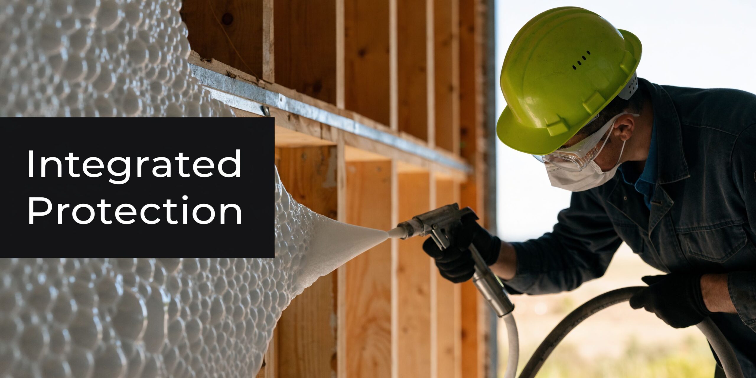 A construction worker wearing safety gear sprays expanding foam insulation onto wooden wall studs at a site.