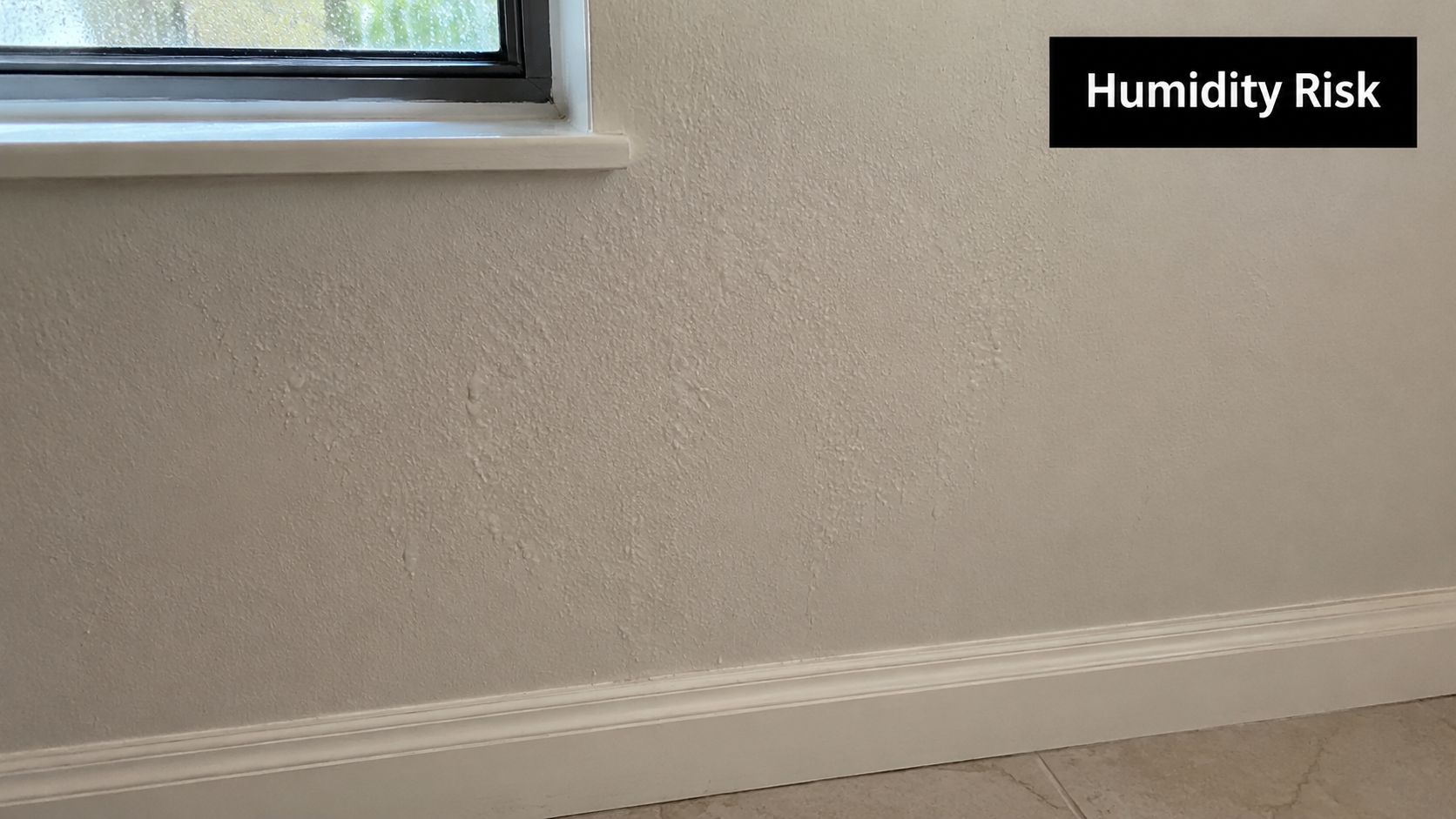 Condensation and moisture droplets forming on a painted interior wall beneath a window frame in a home.